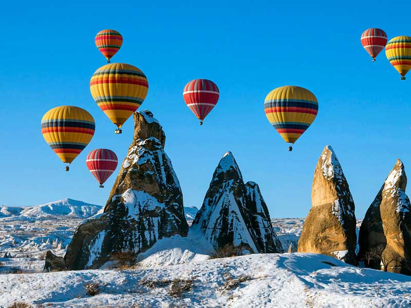 Hot air balloons floating above snow-covered fairy chimneys
